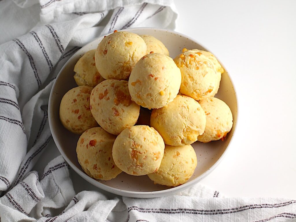 Bowl of golden Gluten Free Brazilian Cheese bread, or Pao de Queijo, stacked on top of each other.
