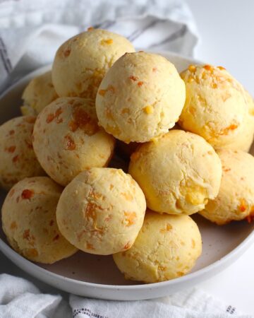 Bowl of golden Gluten Free Brazilian Cheese bread, or Pao de Queijo, stacked on top of each other.