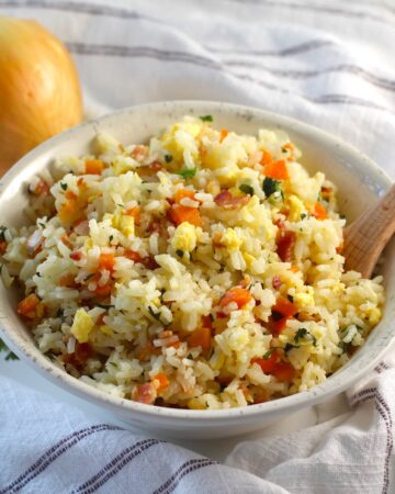 Arroz pilaf in a bowl with carrots, bacon, and cilantro mixed in and a spoon in the bowl.