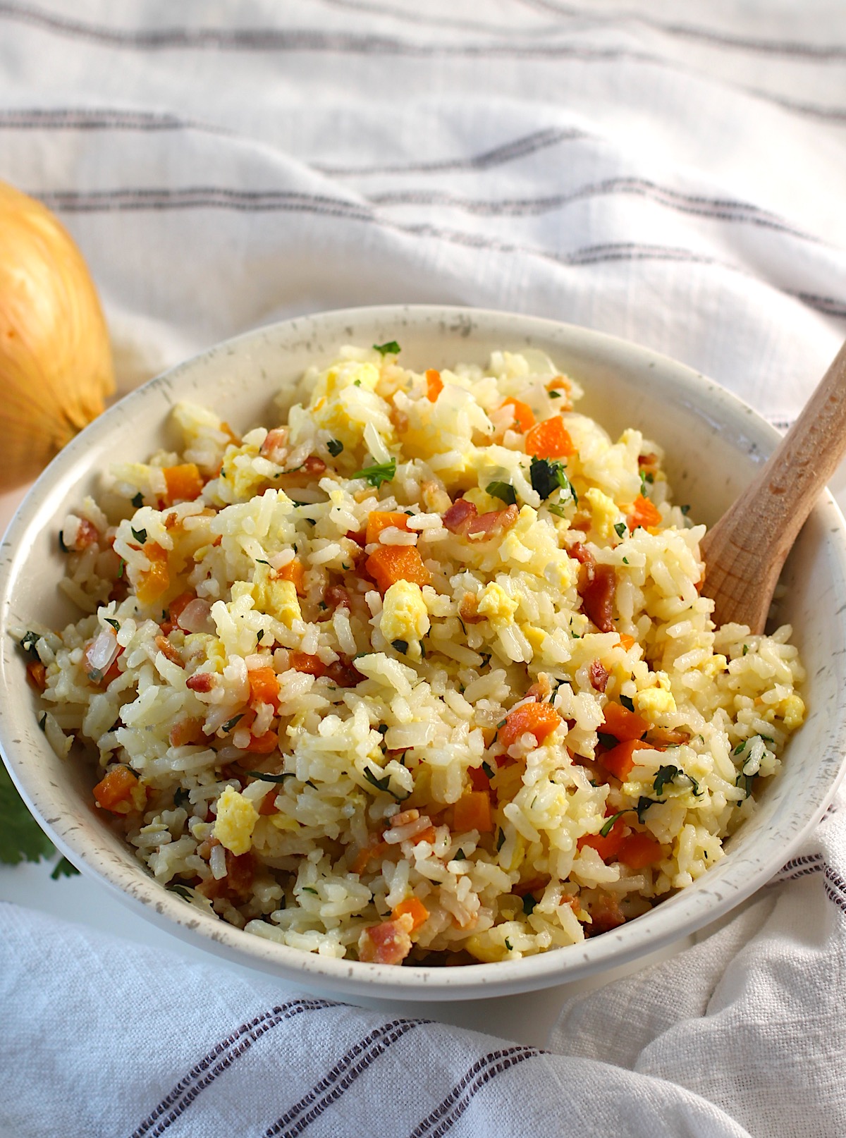 Arroz pilaf in a bowl with carrots, bacon, and cilantro mixed in and a spoon in the bowl.