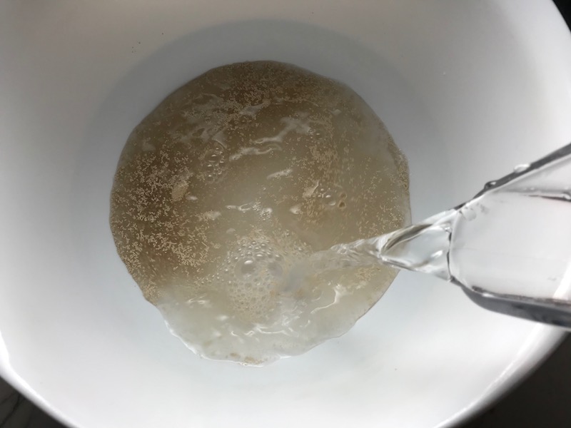 Warm water being poured into a bowl with yeast for Brazilian Pizza dough.