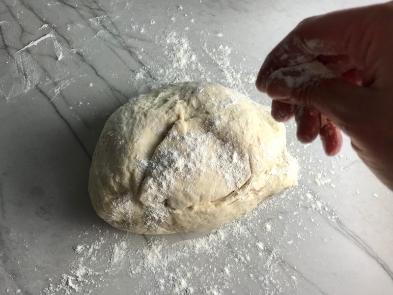 Brazilian Pizza dough on counter with hand sprinkling flour over top before kneading..