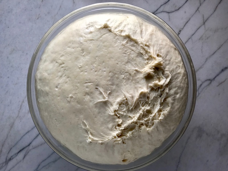 Brazilian Pizza dough risen and doubled in size in glass bowl.