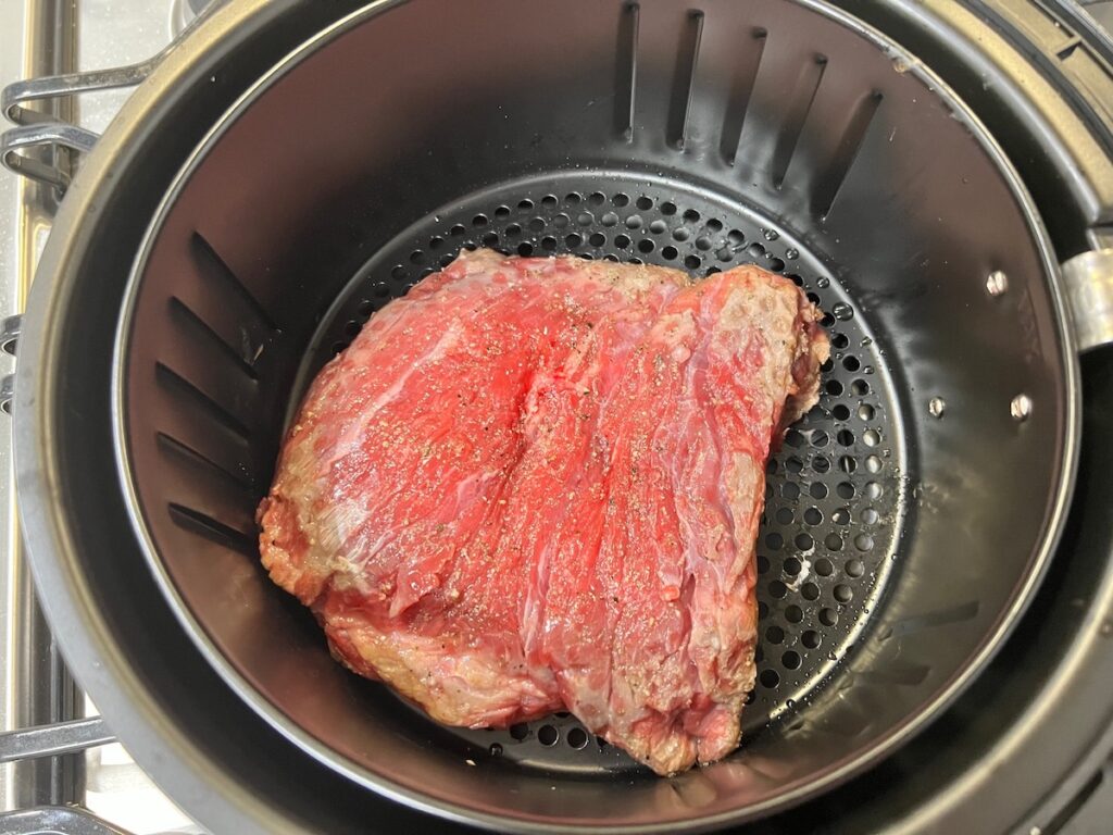 Raw flank steak in an air fryer basket for Churrasco in air fryer recipe.