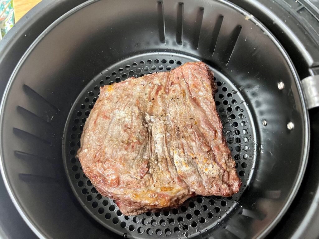 Flank steak flipped over in an air fryer basket for Churrasco in air fryer recipe.