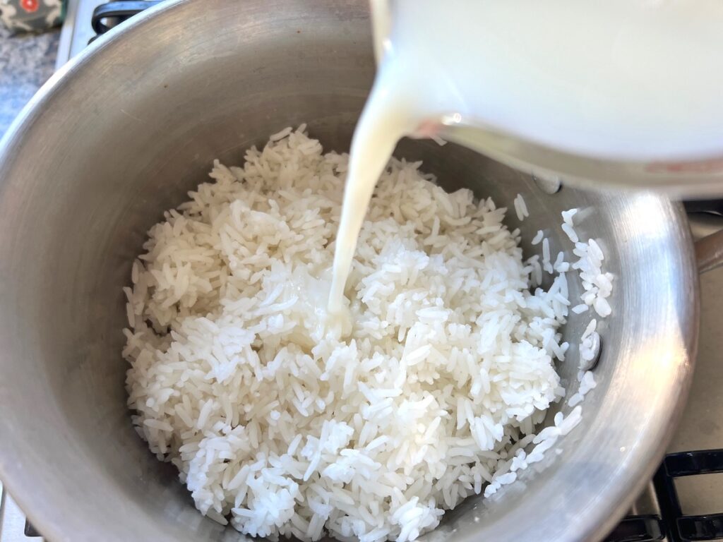 Milking being poured over uncooked white rice in a pot for Rice Pudding with condensed milk.