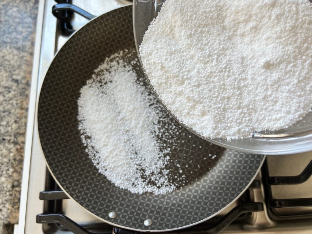 Bowl slowly pouring tapioca starch into a medium frying pan for Brazilian Breakfast Tapioca recipe.