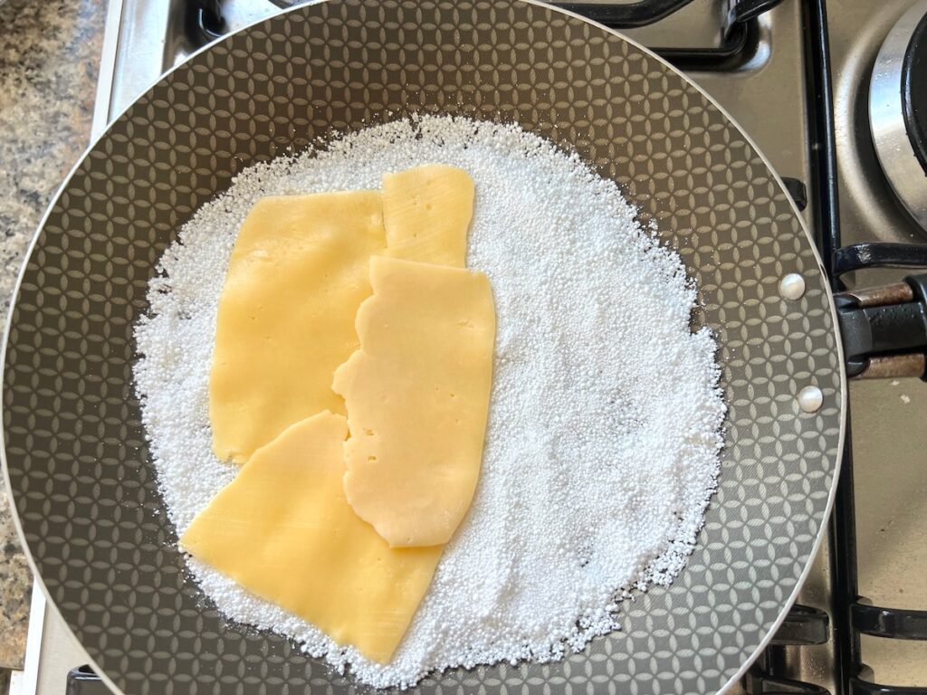 Cheese slices layered onto half of the tapioca starch crepe in a frying pan for Brazilian Breakfast Tapioca recipe.