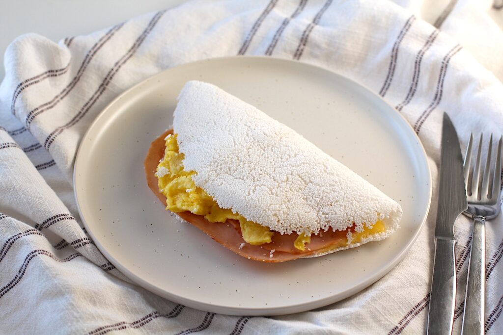 Brazilian Breakfast Tapioca crepe filled with ham, egg, and cheese on the plate on. 