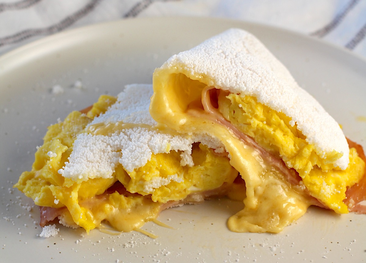 Tapioca filled with ham, egg, and cheese cut in half and stacked with cheese oozing out the front.