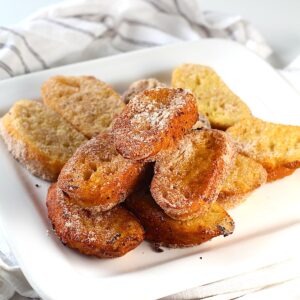 Slices of Brazilian French Toast with condensed milk fried golden brown and dusted with cinnamon sugar stacked on a plate.
