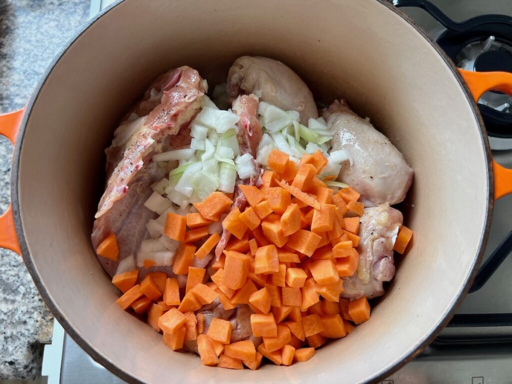 Raw chicken breasts and thighs with bone with diced carrots and onions in a pot for the Canja Brazilian Chicken and Rice Soup recipe.