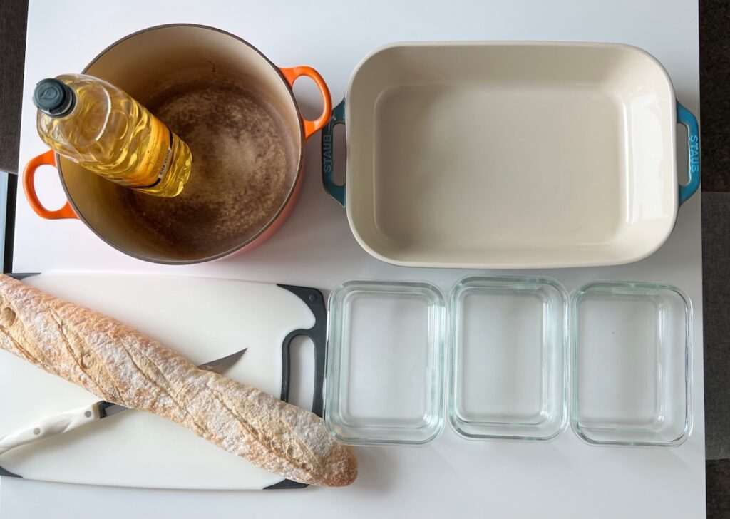 Frying pot, baking dish, 3 smaller dishes, and cutting board with baguette and knife on top for the Brazilian French Toast with condensed milk.