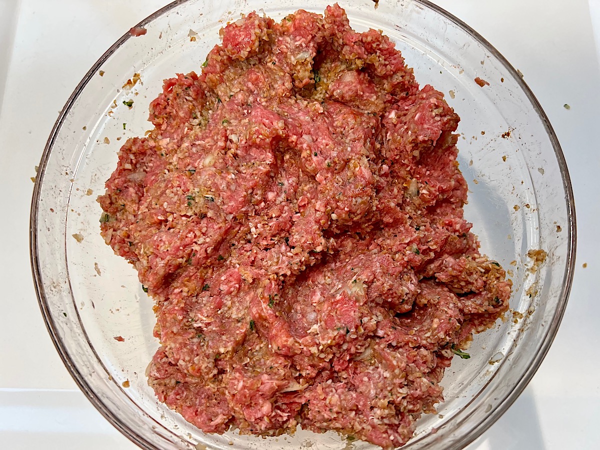 Bowl with mixed raw ground beef, bulgur wheat, seasonings, onions, garlic, and mint for Kibe Mediterranean Ground Beef Kabab recipe.
