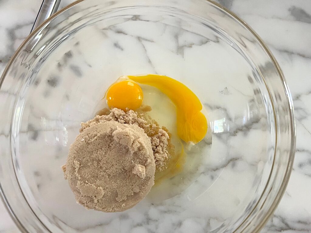 Brown sugar and 2 eggs in a clear glass bowl before being mixed for the Pao de Mel recipe, Brazilian cakes filled with dolce de leite and covered with chocolate.