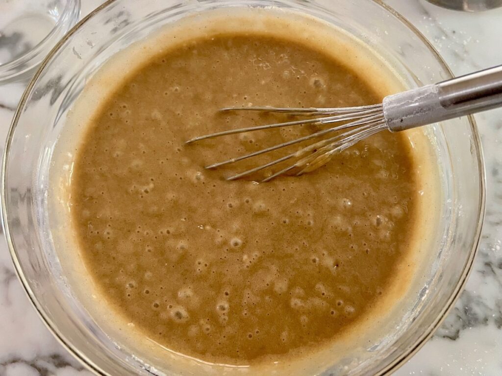 Finished brown batter with whisk in a clear glass bowl for the Pao de Mel recipe, Brazilian cakes filled with dolce de leite and covered with chocolate.