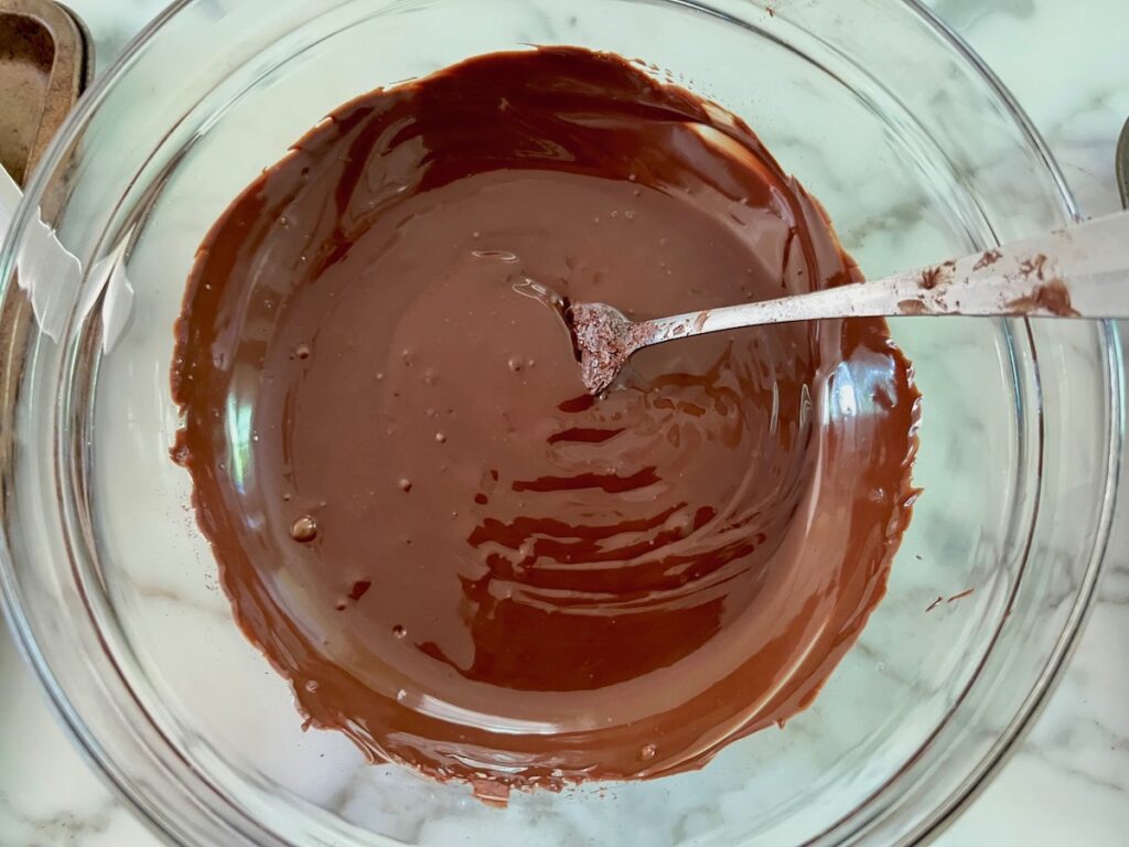 Tempered chocolate in a glass bowl with spoon for the Pao de Mel recipe, Brazilian cakes filled with dolce de leite and covered with chocolate.