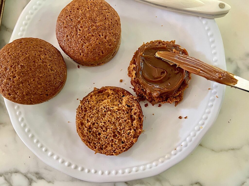Butter knife spreading dulce de leche onto the bottom half of one of the cakes for the Pao de Mel recipe, Brazilian cakes filled with dolce de leite and covered with chocolate.