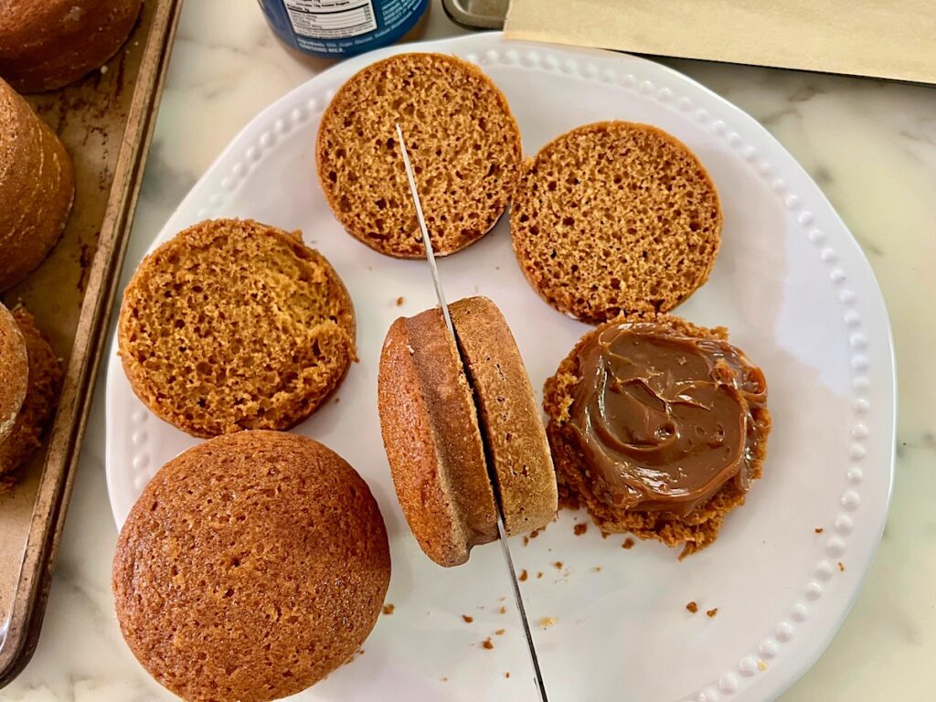 Knife slicing one round cake on it's side in half, like a sandwich bun..
