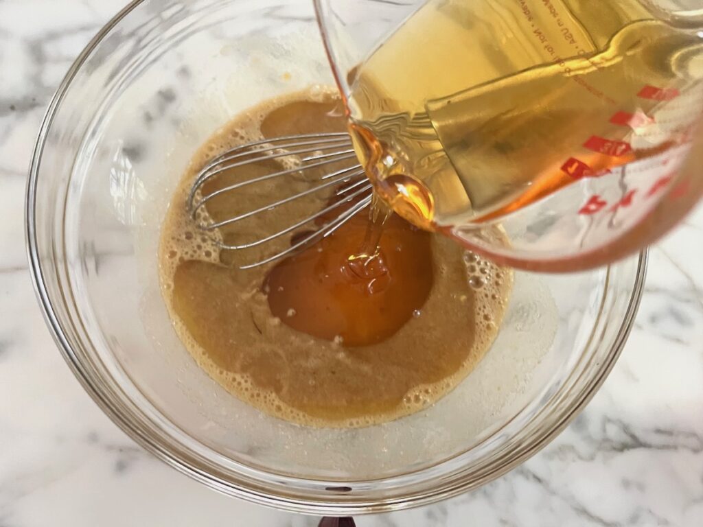 Honey being poured into sugar and eggs in a clear glass bowl for the Honey Loaf recipe.