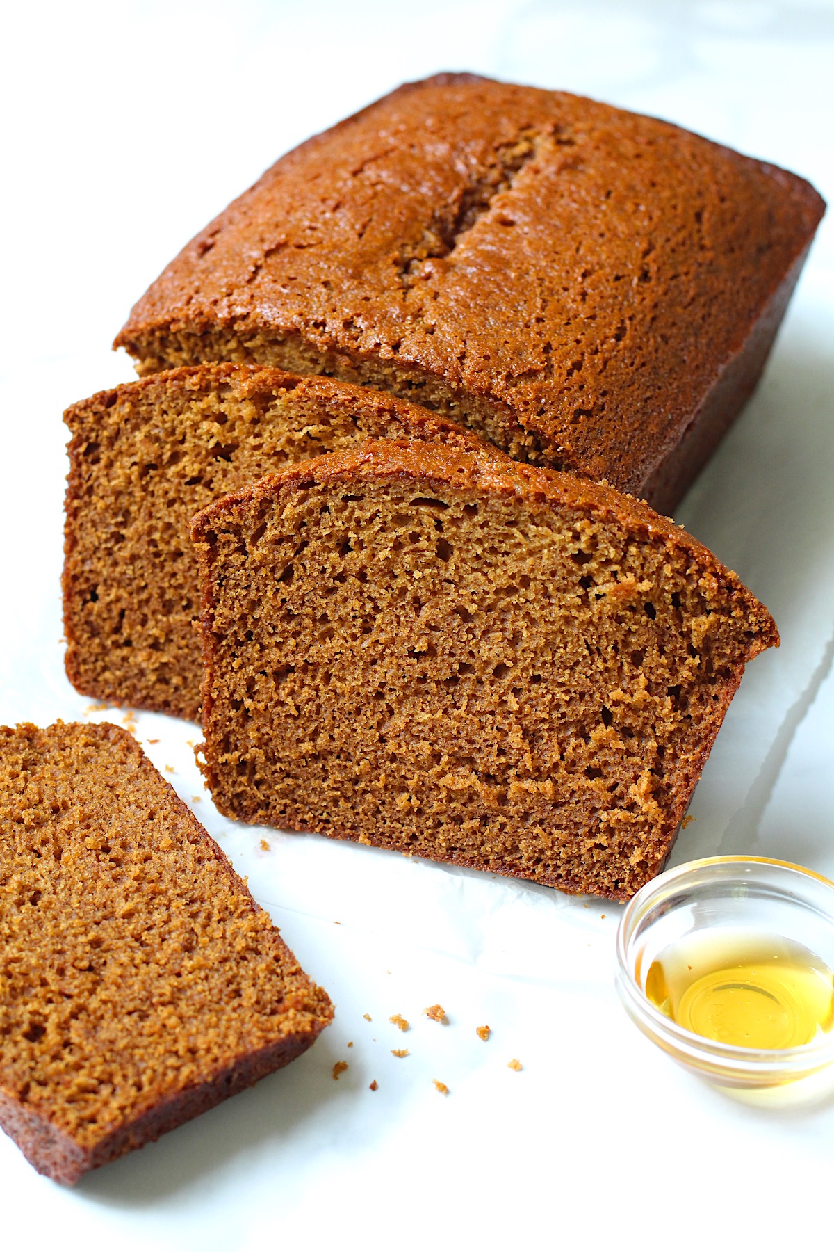 Honey Loaf cake baked beautifully golden brown on table with 3 slices standing in front showing the moist inside.  On the counter is a small bowl of honey.