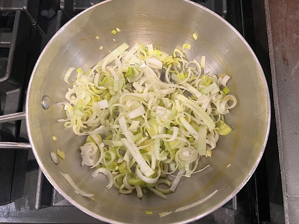 Sliced leeks cooking in a pot with olive oil for the filling for the Ham and Leek Pie.
