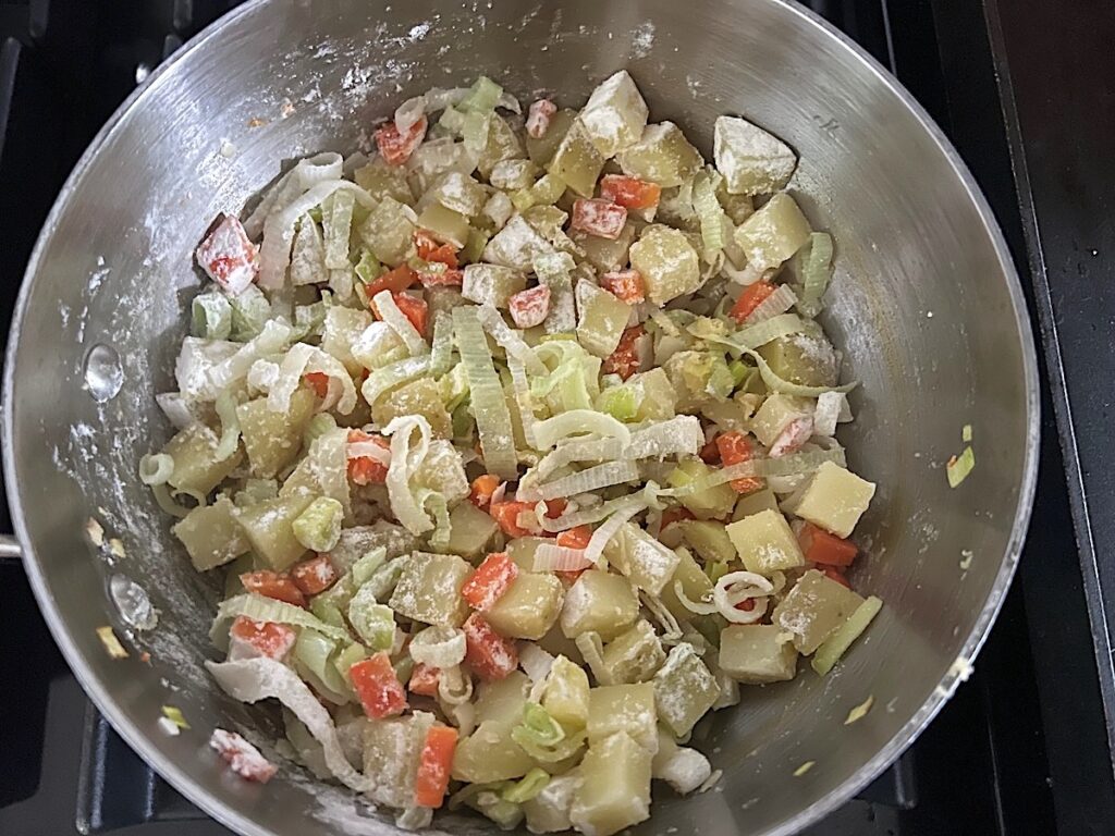 Pre-cooked carrots and potatoes added to sliced leeks and combined with flour in a pot for the filling for the Ham and Leek Pie.