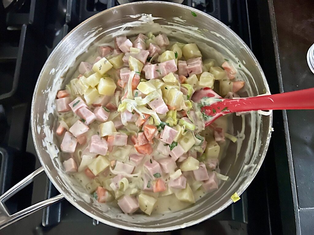 To the thickened sauce, the Ham, Dijon mustard, Thyme, Parsley, and half and half are mixed in for the Ham and Leek Pie.