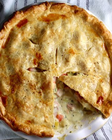 Ham and Leek Pie with potatoes and carrots in a cream sauce and flaky golden brown pie crust on top. Pie in pie pan on counter with 1 slice removed showing creamy, savory filling.