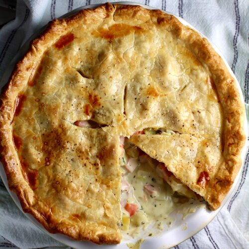 Ham and Leek Pie with potatoes and carrots in a cream sauce and flaky golden brown pie crust on top. Pie in pie pan on counter with 1 slice removed showing creamy, savory filling.