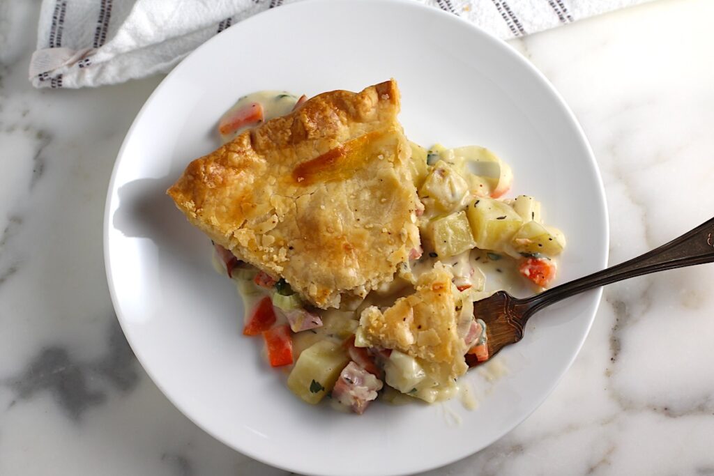 Ham and Leek Pie piece on a plate with fork with potatoes and carrots in a cream sauce and flaky golden brown pie crust on top.