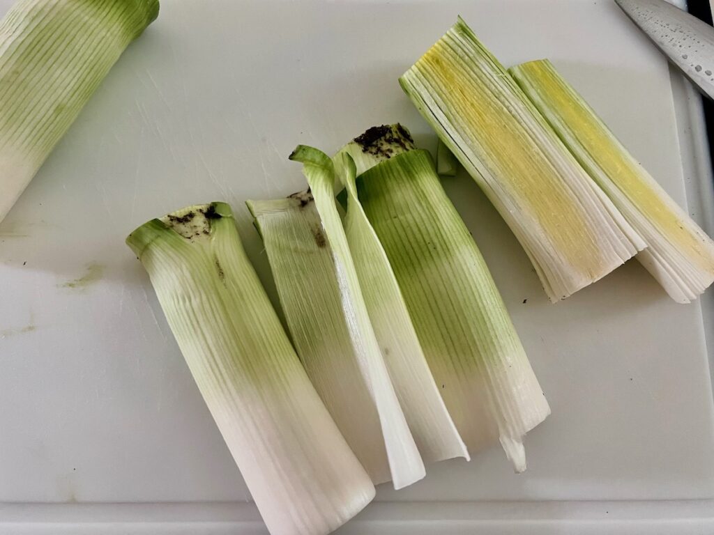 Raw white ends of 2 leeks cut in half lengthwise on cutting board for the Ham and Leek Pie.