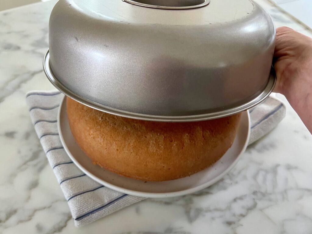 Baked Cornmeal cake being turned out upside down onto a plate on the counter for this Bolo de Fuba, Cornmeal Cake, recipe.