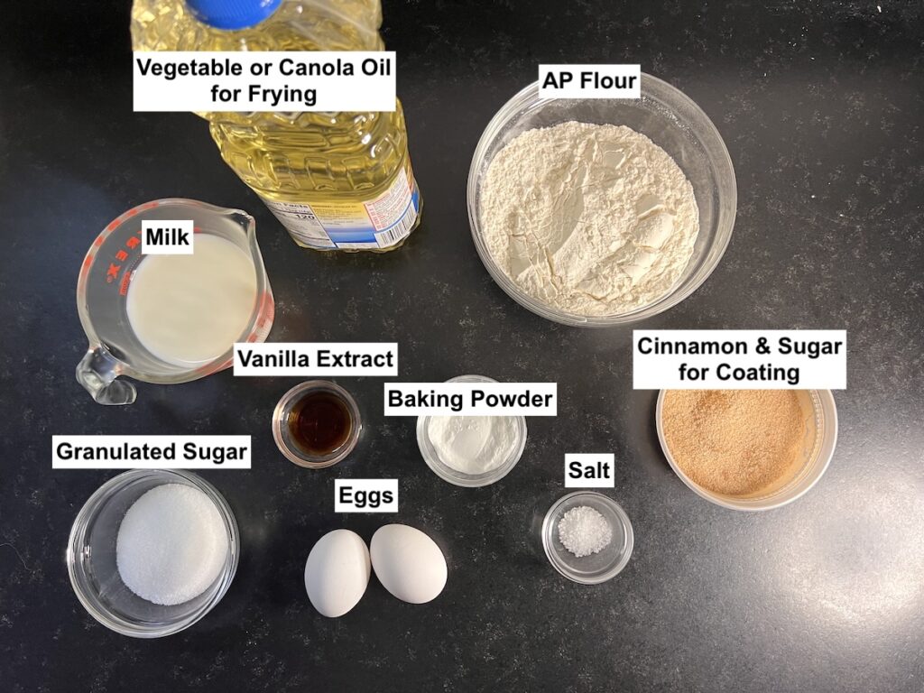 All ingredients measure out in bowls on counter and labeled for the Bolinhos de Chuva Recipe (Donut holes with Cinnamon Sugar coating).