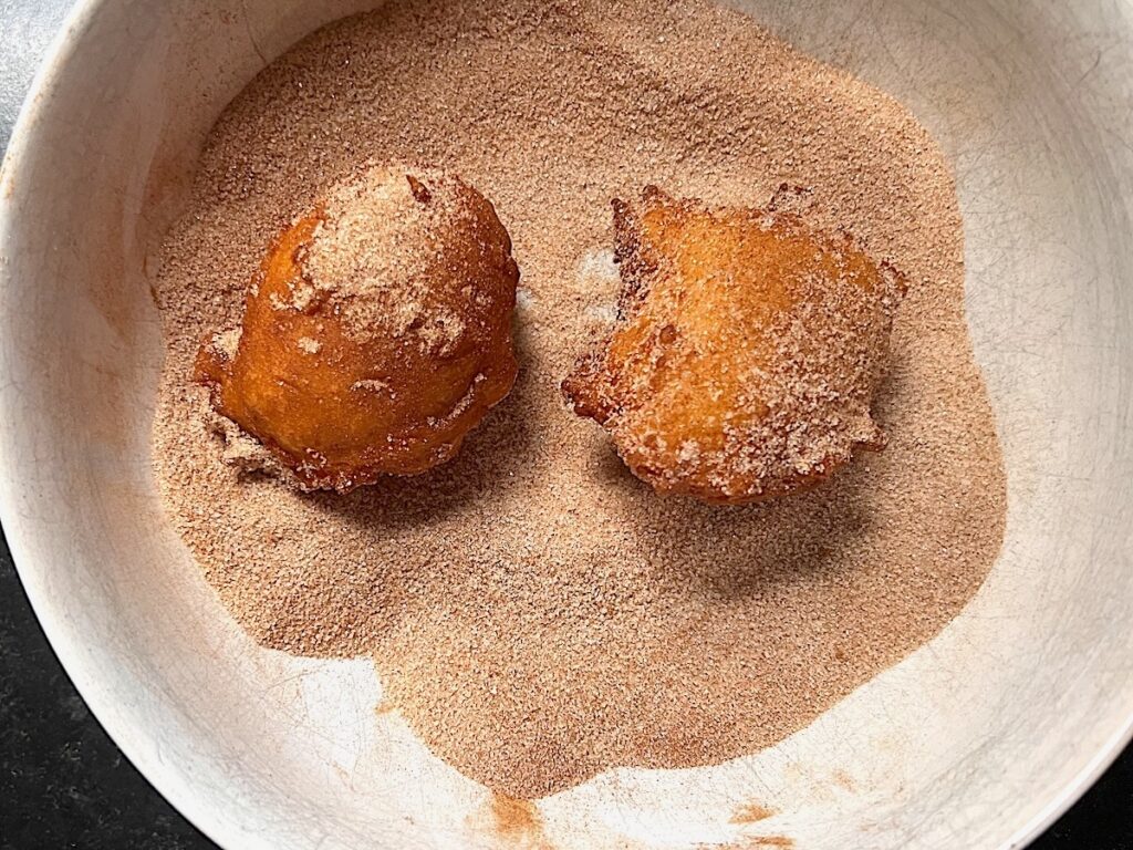 2 bolinhos being rolled and coated in a cinnamon sugar mixture.